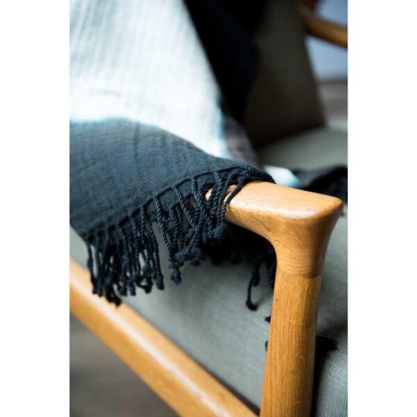 The Bloom & Give black and beige merino wool throw is folded up on a wooden chair. Bloom & Give has a strong fair trade commitment and donates half of their profits to girls' education programs.