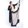The Bloom & Give merino wool throw is being held by a model. The throw has hand dyed and have a black perimeter, black tassles, and a white or beige middle.