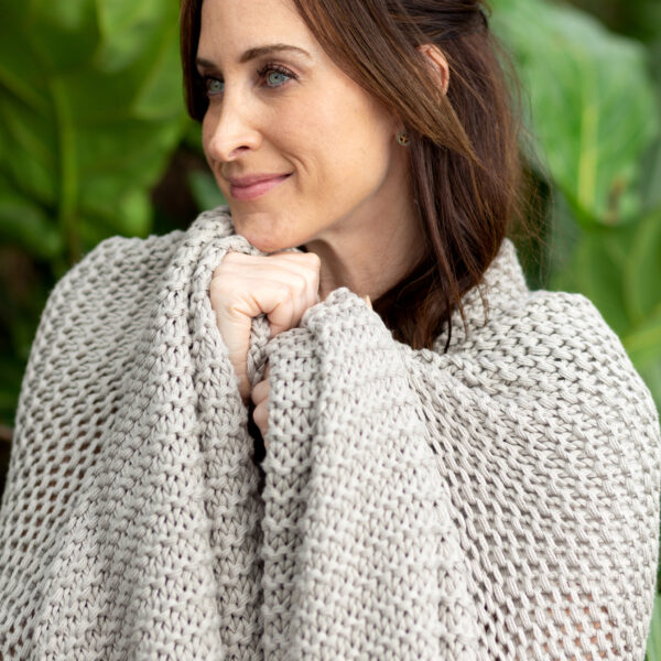 Woman wrapped in sustainable organic cotton grey knit blanket throw from women-owned Zestt Organics