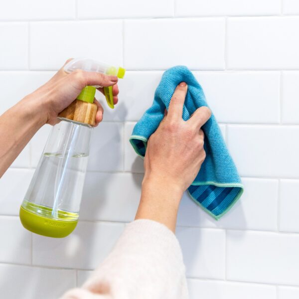 Glass spray bottle with blue recycled microfiber cleaning cloth for sustainable cleaning products on white shower tile