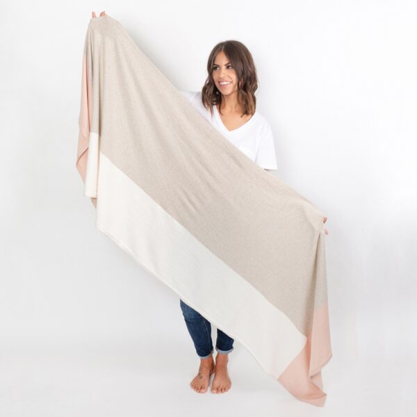 Photo shows a model holding up the versatile and earth-friendly Zestt Organics travel scarf in blush color block to show tan, white, and blush coloring.