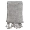 The knitted throw by Zestt Organics is shown folded up, displaying details of its large knitted gauge and beautiful twisted tassels.