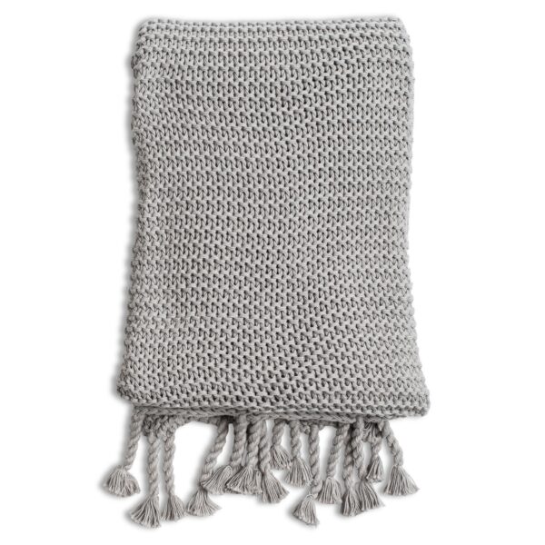 The knitted throw by Zestt Organics is shown folded up, displaying details of its large knitted gauge and beautiful twisted tassels.