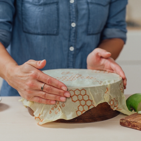 Photo shows a model warming her hands around the top of a bowl with a Bee's Wrap eco-friendly food wrap. Keeping the wrap warm allows the product to be bent and contorted around the top of the bowl.