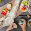 A Bee's Wrap bread wrap is a perfect way to transport bread on the way to a picnic. A charcutterie plate is shown here, with olives, grapes, cheese, and bread, wrapped in the Bee's Wrap bread wrap.