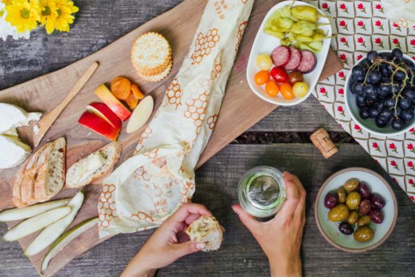 A Bee's Wrap bread wrap is a perfect way to transport bread on the way to a picnic. A charcutterie plate is shown here, with olives, grapes, cheese, and bread, wrapped in the Bee's Wrap bread wrap.