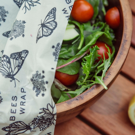 A close-up of a wooden salad bowl, covered by the monarch printed, earth-friendly Bee's Wrap beeswax food wrap.