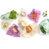 Photo shows the eco-friendly Beeswrap brand food wraps sitting on a counter in a variety of sizes and colors, a part of the 7 piece variety pack with honeycomb, clover, and geometric designs.