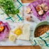 Photo shows the eco-friendly Beeswrap brand food wraps sitting on a counter in a variety of sizes and colors, a part of the 7 piece variety pack with honeycomb, clover, and geometric designs.