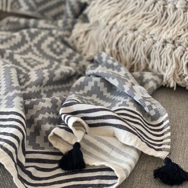 Close-up of the eco-friendly Hilana Merida Gray Turkish towel, showing black tassels, and gray and white stepped diamond pattern.