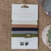 Kooshoo brand hair ties, shown in 5 naturally classic colors (white, pink, navy, gray, and green), are sitting on paper packaging. Kooshoo hair ties are organic and biodegradable, fair trade and fair rubber.