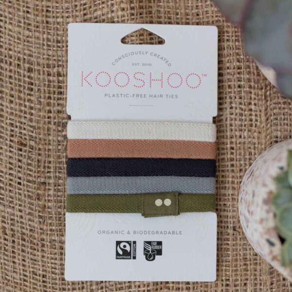 Kooshoo brand hair ties, shown in 5 naturally classic colors (white, pink, navy, gray, and green), are sitting on paper packaging. Kooshoo hair ties are organic and biodegradable, fair trade and fair rubber.