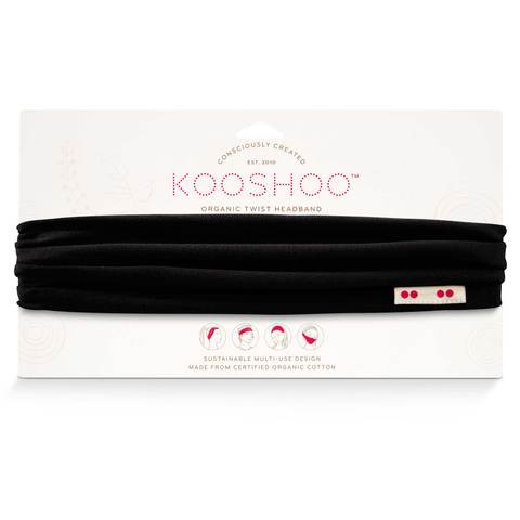 A raven black Kooshoo brand twist headband, made with organic cotton, is shown on display with its FSC certified compostable paper packaging.