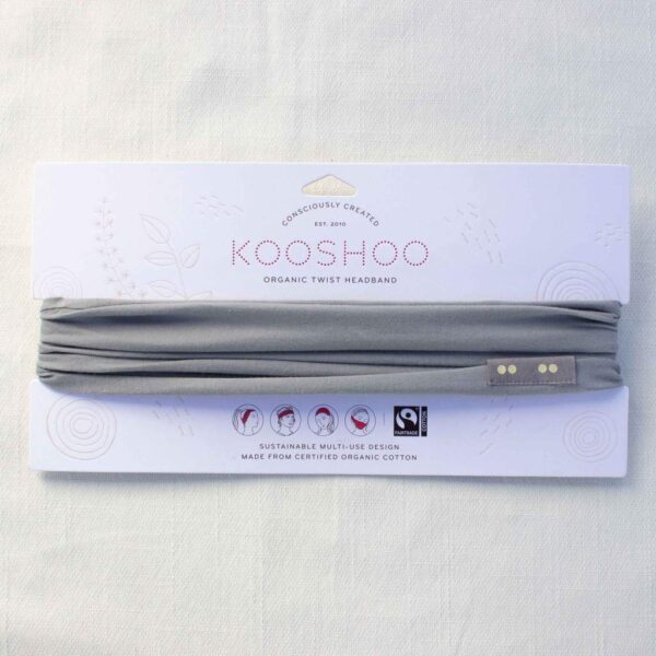 A grounding gray Kooshoo brand twist headband, made with organic cotton, is shown on display with its FSC certified compostable paper packaging.