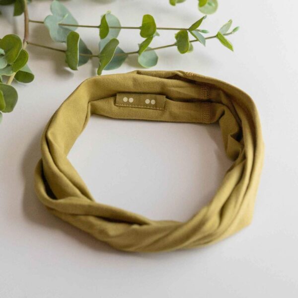 A Kooshoo twist headband shown in safari green; made from organic cotton and locally dyed, cut, and sewn in a fair trade certified Los Angeles facility