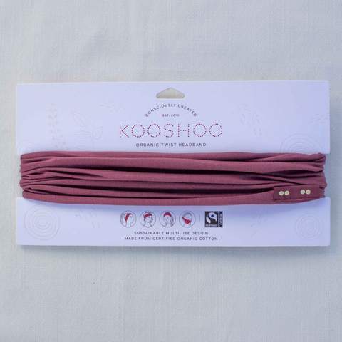A wild ginger Kooshoo brand twist headband, made with organic cotton, is shown on display with its FSC certified compostable paper packaging.