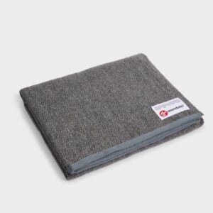 This sustainably made yoga blanket by Manduka is constructed from all recycled fibers; shown folded in sediment gray.