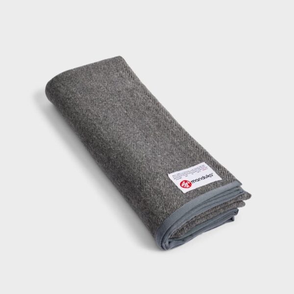 This sustainably made yoga blanket by Manduka is constructed from all recycled fibers; shown folded in sediment gray.