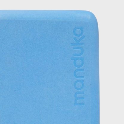 A close-up of the eco-friendly Manduka mini yoga block, showing the small 'Manduka' brand name etched into the foam.