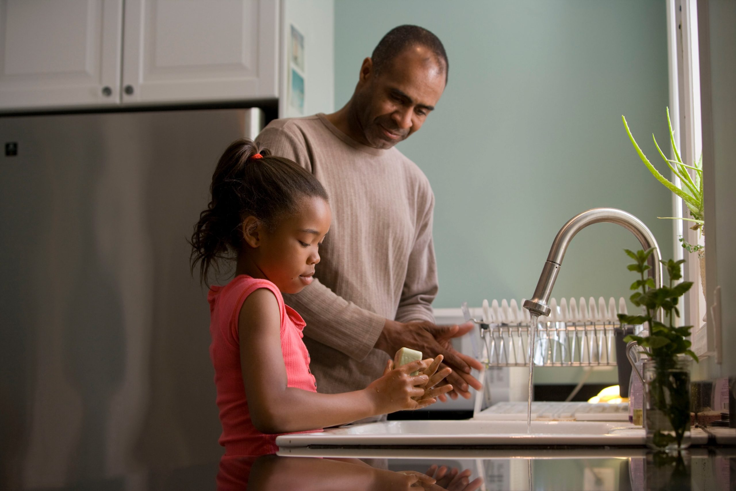 A father and daughter washing hands in kitchen sink for eco-friendly teaching blog