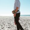 A male model on the beach, wearing his Packster hip pack from Green Guru in Earthtone colors. Hip packs are great for hiking, running, or a fun beach day!