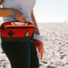 Close up of a model wearing the eco-friendly Packster hip pack by Green Guru at the beach. A perfect bag for your keys, phone, and snacks on your next beach adventure.