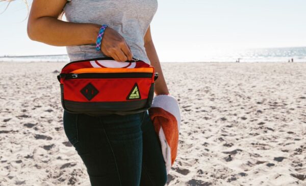 Close up of a model wearing the eco-friendly Packster hip pack by Green Guru at the beach. A perfect bag for your keys, phone, and snacks on your next beach adventure.