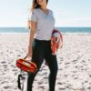 A model at the beach holding her earth-friendly Packster hip pack, by Green Guru, by the top carrying strap. Comes in fun and wild neon colors.