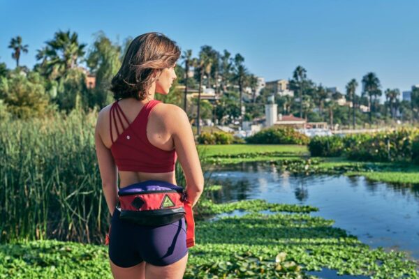 Female model, taking a break from her run, is wearing the Tripster eco-friendly hip pack by Green Guru around her waist.