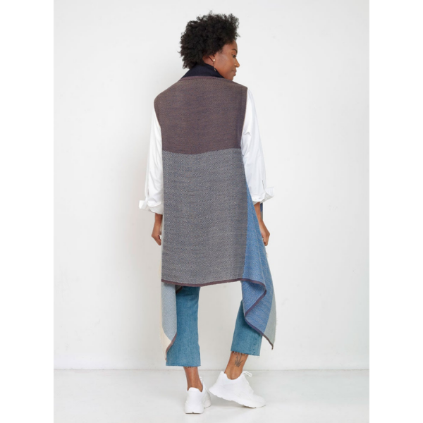 A model is modeling the back of the Cape Infinity by Fifth Origins in sky blue, made with 100% organic wool. The purchase of each cape supports women artisans.