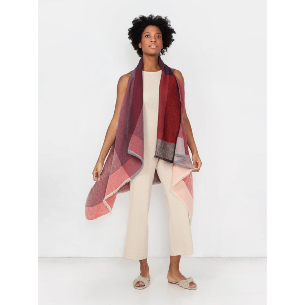 The organic Cape Infinity by Fifth Origins, shown here on a model in tulip red, is woven in a color block pattern and is made sustainably by women artisans in India.