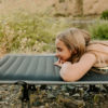 Young woman on foldable camping travel cot near mountain
