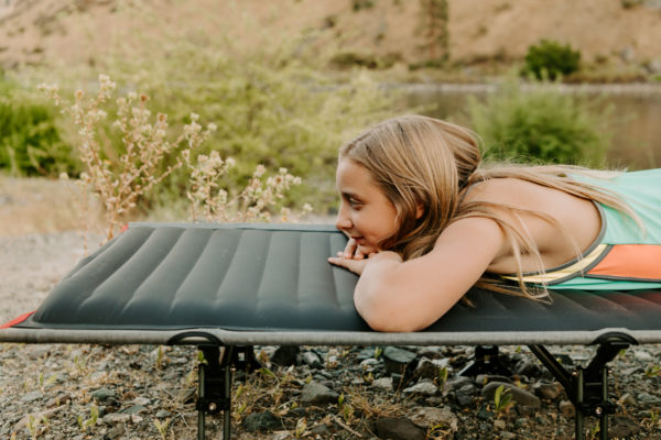 Young woman on foldable camping travel cot near mountain