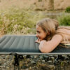 Young woman on foldable camping travel cot near mountain