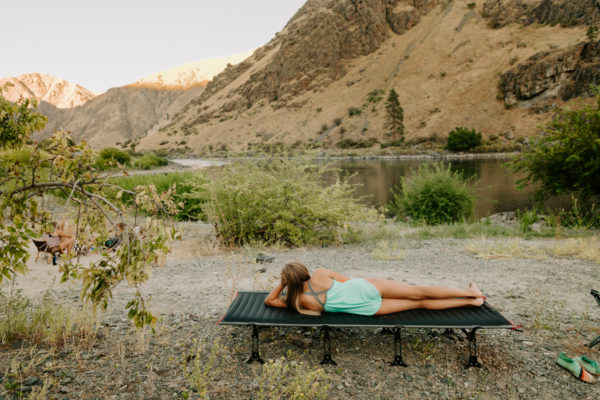 Young woman on foldable camping travel cot near mountain