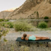 Young woman on foldable camping travel cot near mountain