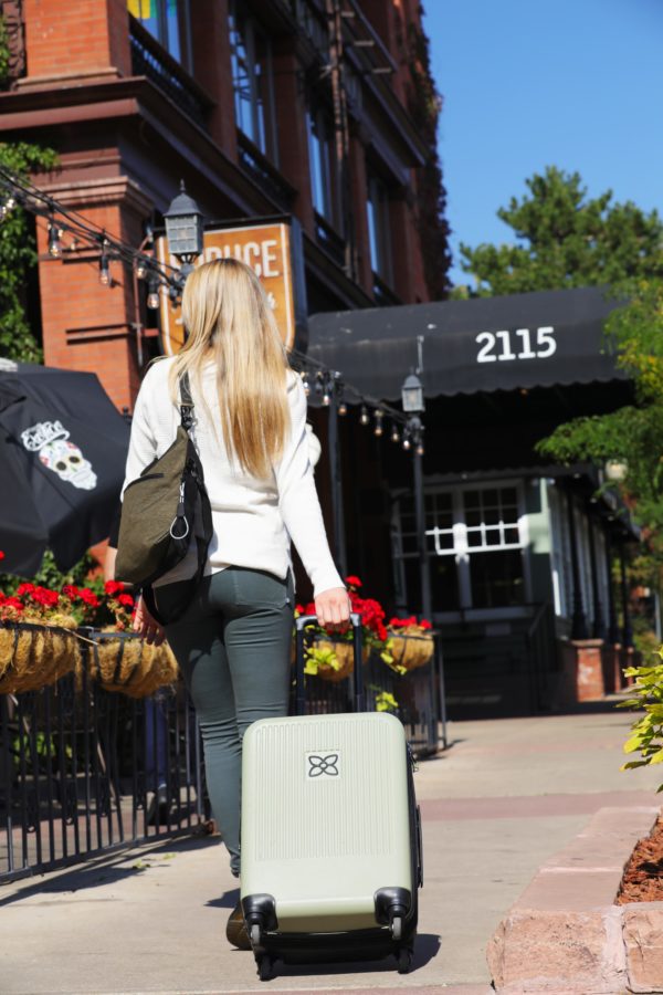 Model is shown walking toward her hotel on the sidewalk, pulling her Meridian luggage in sage, by Sherpani. This luggage is sturdy, lightweight, and has an anti-crush exterior.