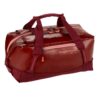 The migrate duffel bag by Eagle Creek, shown here in burnt berry, is a 40 liter duffel bag with dark red fabric and pink zippers that is made from durable and weather-proof recycled materials.