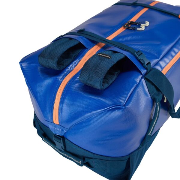 The sustainable migrate duffel bag by Eagle Creek, shown here in mesa blue, is a 90 liter duffel bag with blue fabric, orange zippers, and navy straps that has versatile backback straps that can be tucked away when not in use.