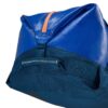 The sustainable migrate duffel bag by Eagle Creek, shown here in mesa blue, is a 90 liter duffel bag with blue fabric, orange zippers, and navy straps. The bag can be clipped down to save space, or unclipped to create extra packing capacity.