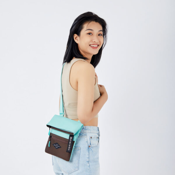 The sustainably made Sherpani Pica crossbody bag, made from 100% recycled materials, is shown here in a colorblock with Seagreen and Brown and seagreen zipper pulls.