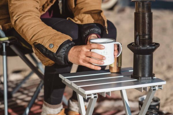 Person putting camping coffee on portable, aluminum Canyon side table