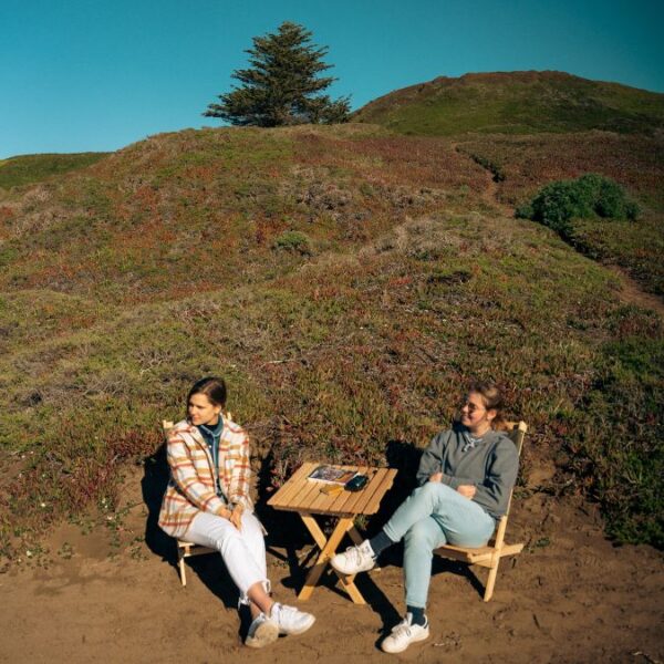 Two young women sitting in sustainably-made outdoor wood travel chairs and table