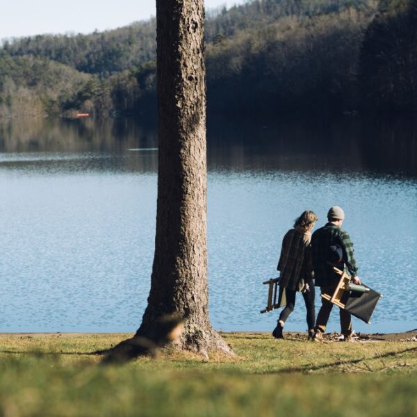 Couple carrying sustainable wood, foldable chairs near lake