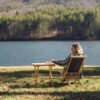 View of women in front of lake in sustainable wood, folding chair and table set for travel and campaing