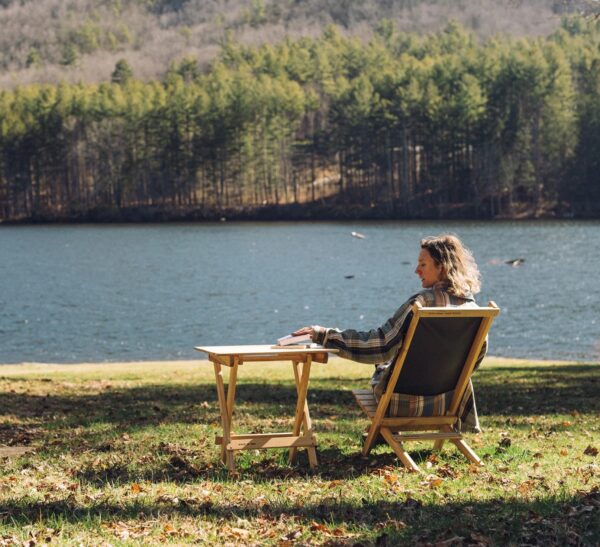 View of women in front of lake in sustainable wood, folding chair and table set for travel and campaing