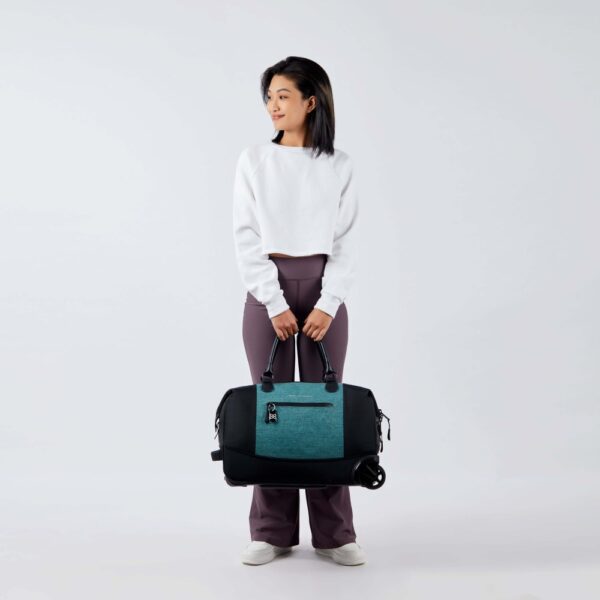 The Trip rolling duffel bag, shown here in teal and black, is made of recycled fabrics. The handle of this sustainable roller bag is collapsible while being used as a duffel bag.