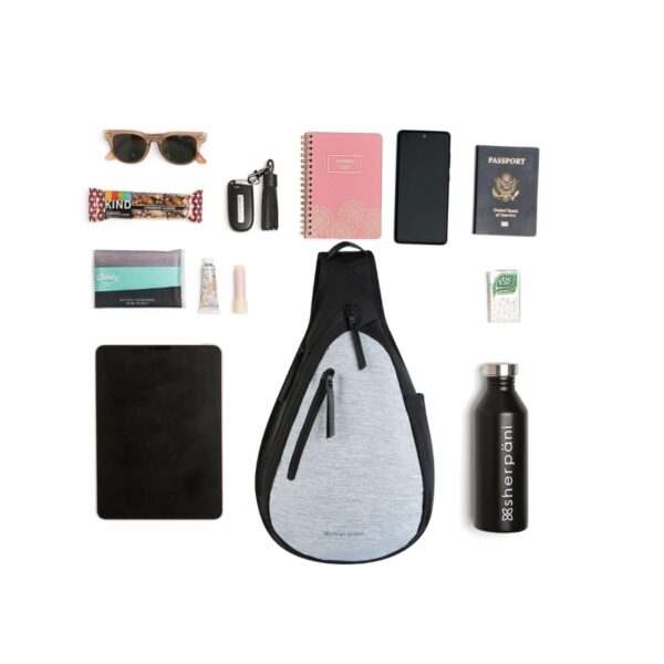 This image shows all of the contents an Esprit AT bag can hold. The image includes the following items laid out next to the bag: sun glasses, a Kind bar, a small travel-sized bag of Kleenex, chapstick and a mini lotion, a small tablet, a Sherpani water bottle, a passport, a small notebook, a cell phone, a box of Tic Tac and a key ring.
