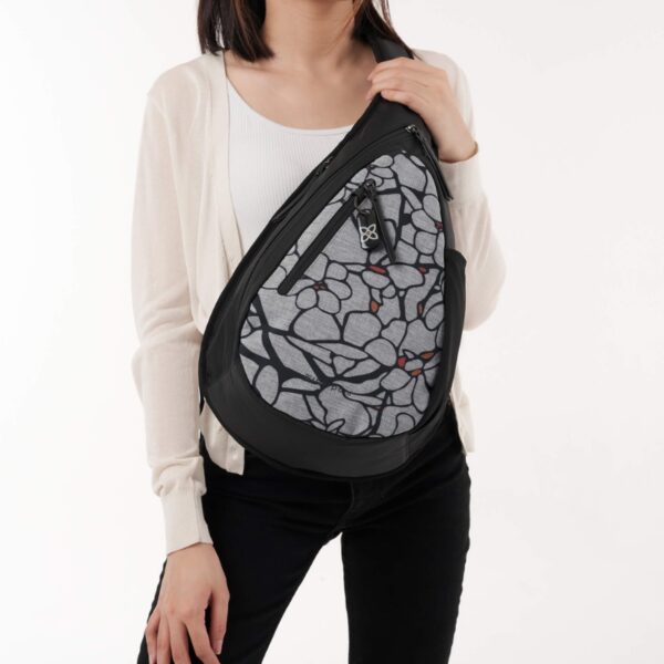 The Esprit AT Shoulder Sling Bag is shown here with someone wearing the Sakura pattern from a frontal view. In this case, she slung it over her torso and put the strap on her back. The pack extends across her body from her shoulder to her waist.