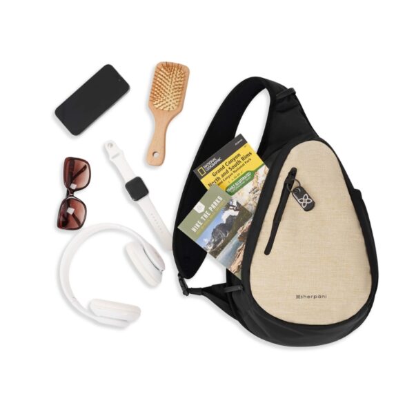 This image shows the Esprit AT Shoulder Sling Bag in straw. The bag has an open zipper with several items next to it, indicating items that were in the bag. This includes a hair brush, a watch, sun glasses, a cell phone and some head phones.